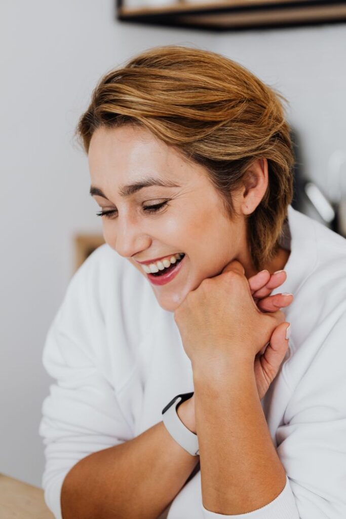 A joyful woman with short hair laughing indoors, showing warmth and positivity.